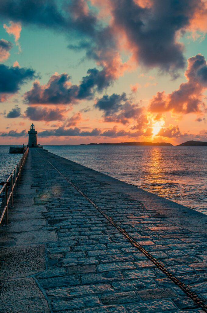 Scenic sunset over a lighthouse and paved walkway in Guernsey. Ideal for travel and nature themes.