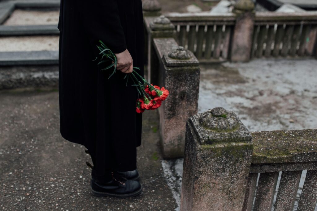 A somber scene of a person holding red flowers near a tombstone at a cemetery.