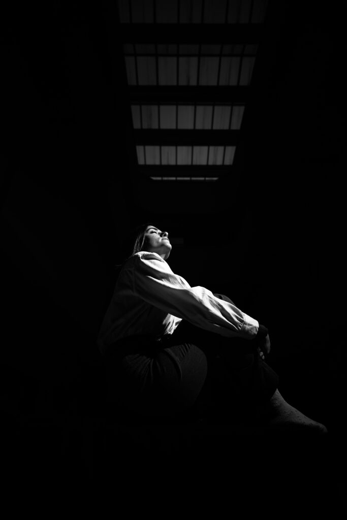 A striking black and white photo of a woman seated in dramatic shadows, conveying intimacy and depth.