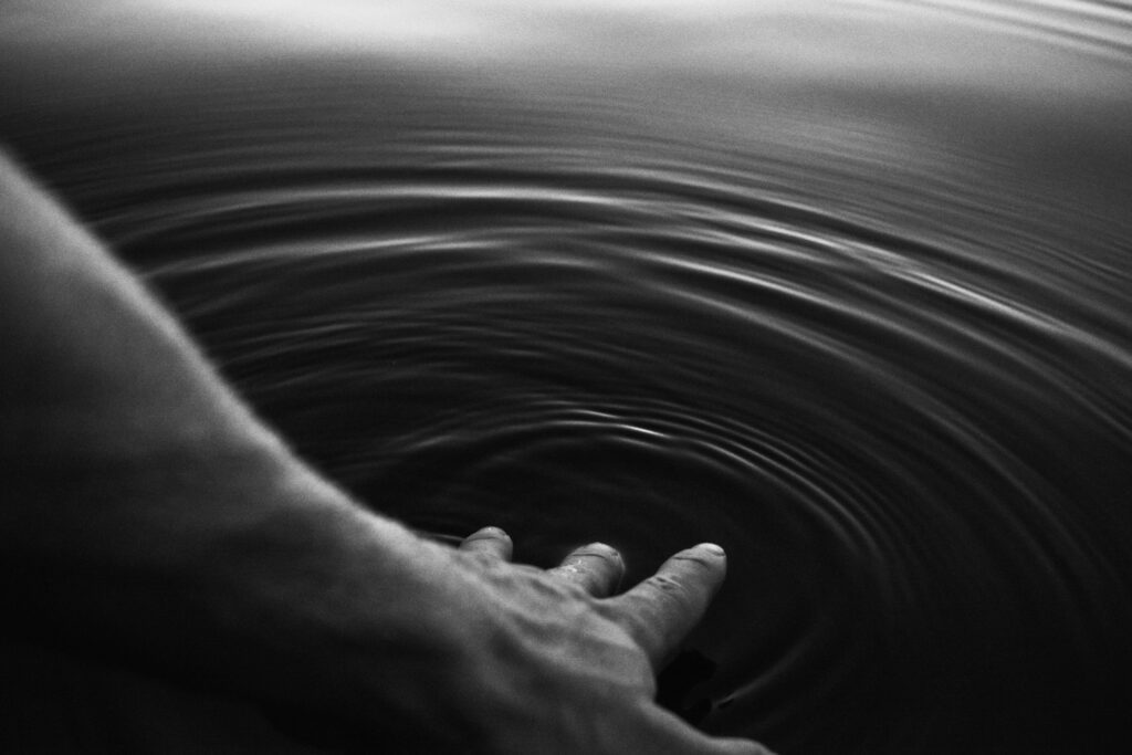 Black and white image of a hand creating ripples in the water, evoking calmness.