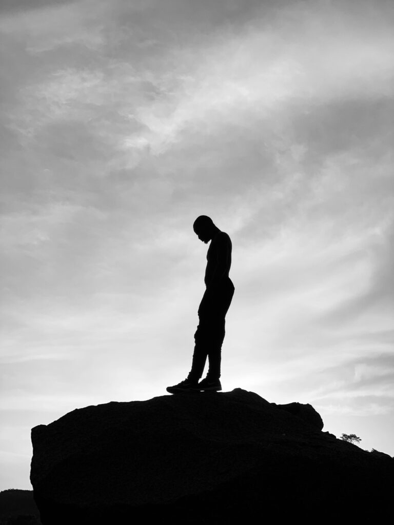 Dramatic silhouette of a man on a rock against a twilight sky, evoking introspection.