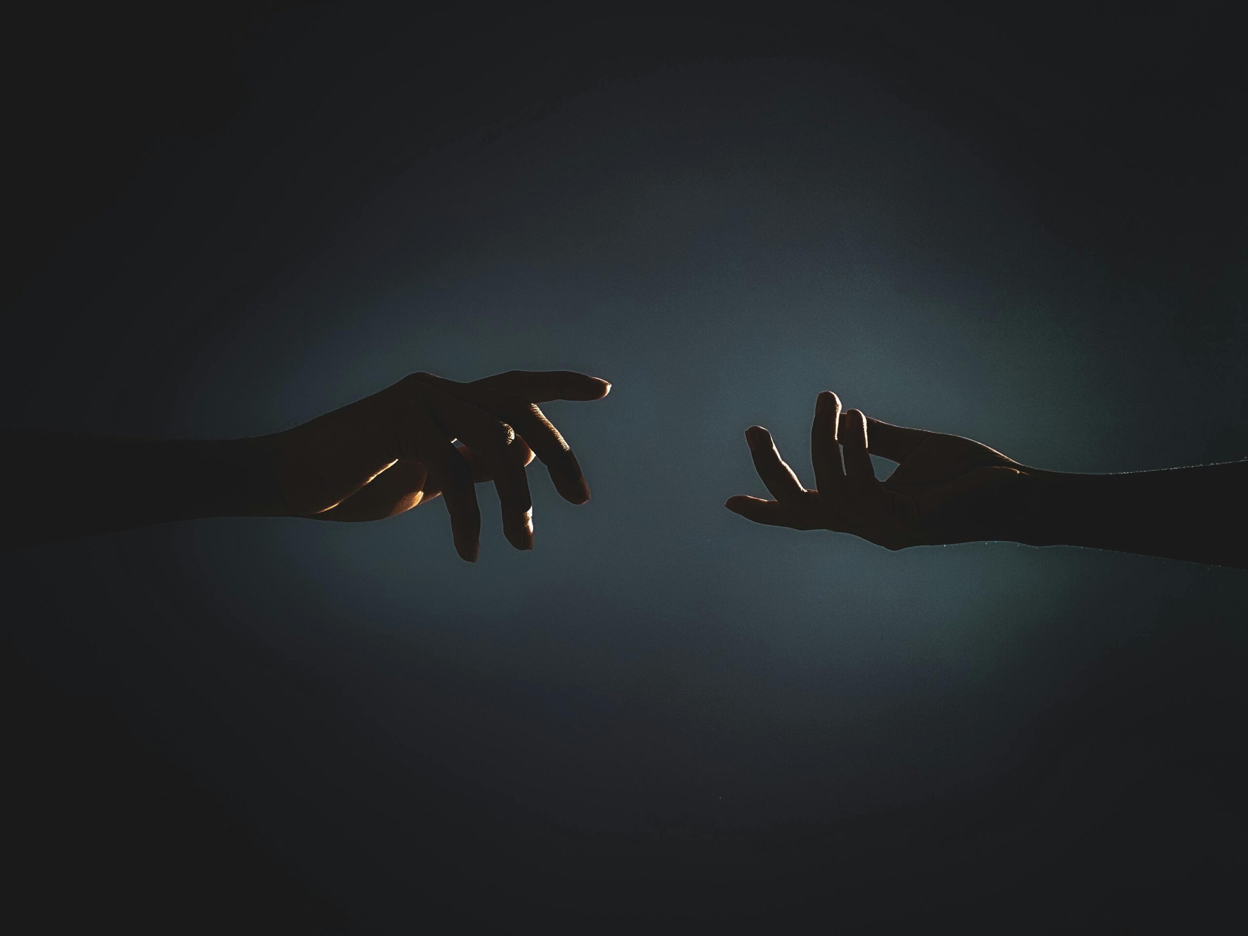 Dramatic silhouette of hands reaching towards each other in a dark setting, symbolizing connection.