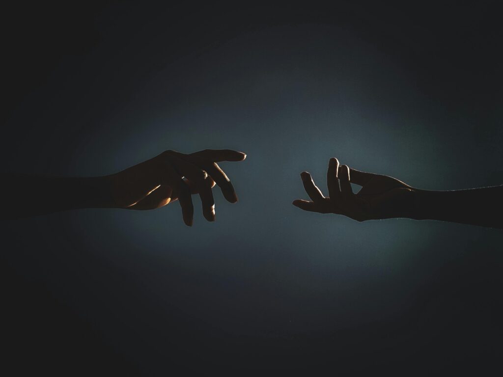 Dramatic silhouette of hands reaching towards each other in a dark setting, symbolizing connection.