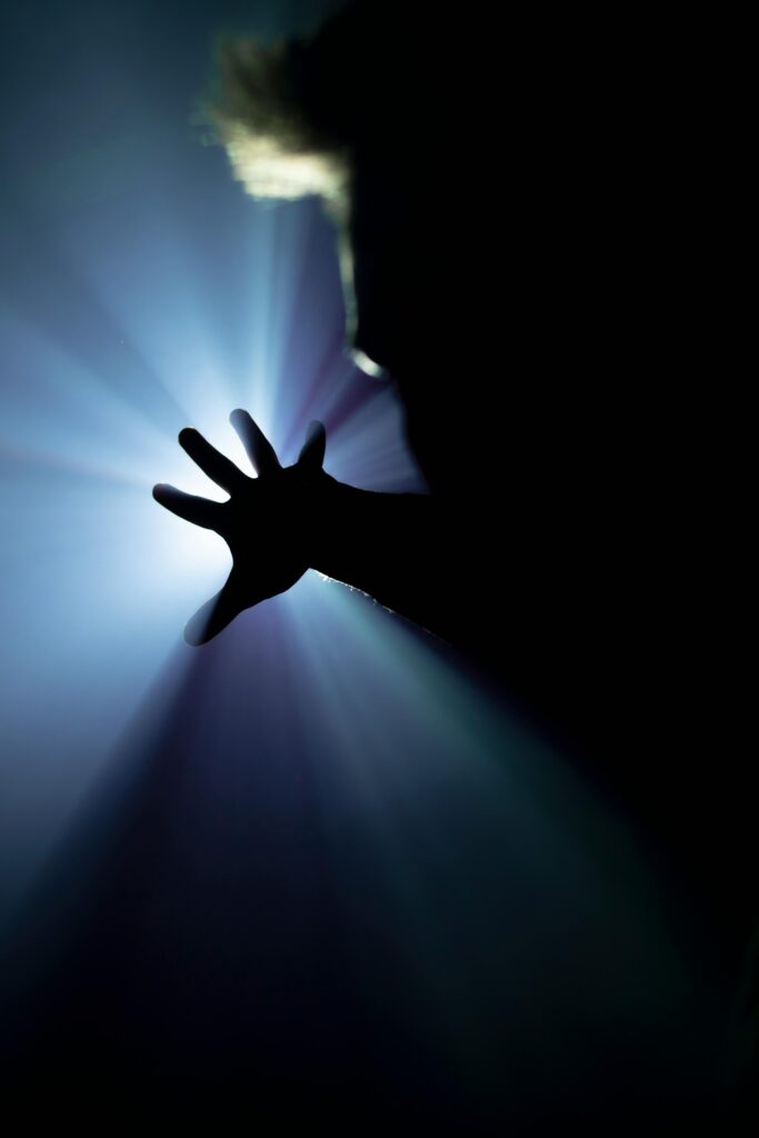 Silhouette of a hand reaching towards a bright mystical light, creating a dramatic and artistic scene.